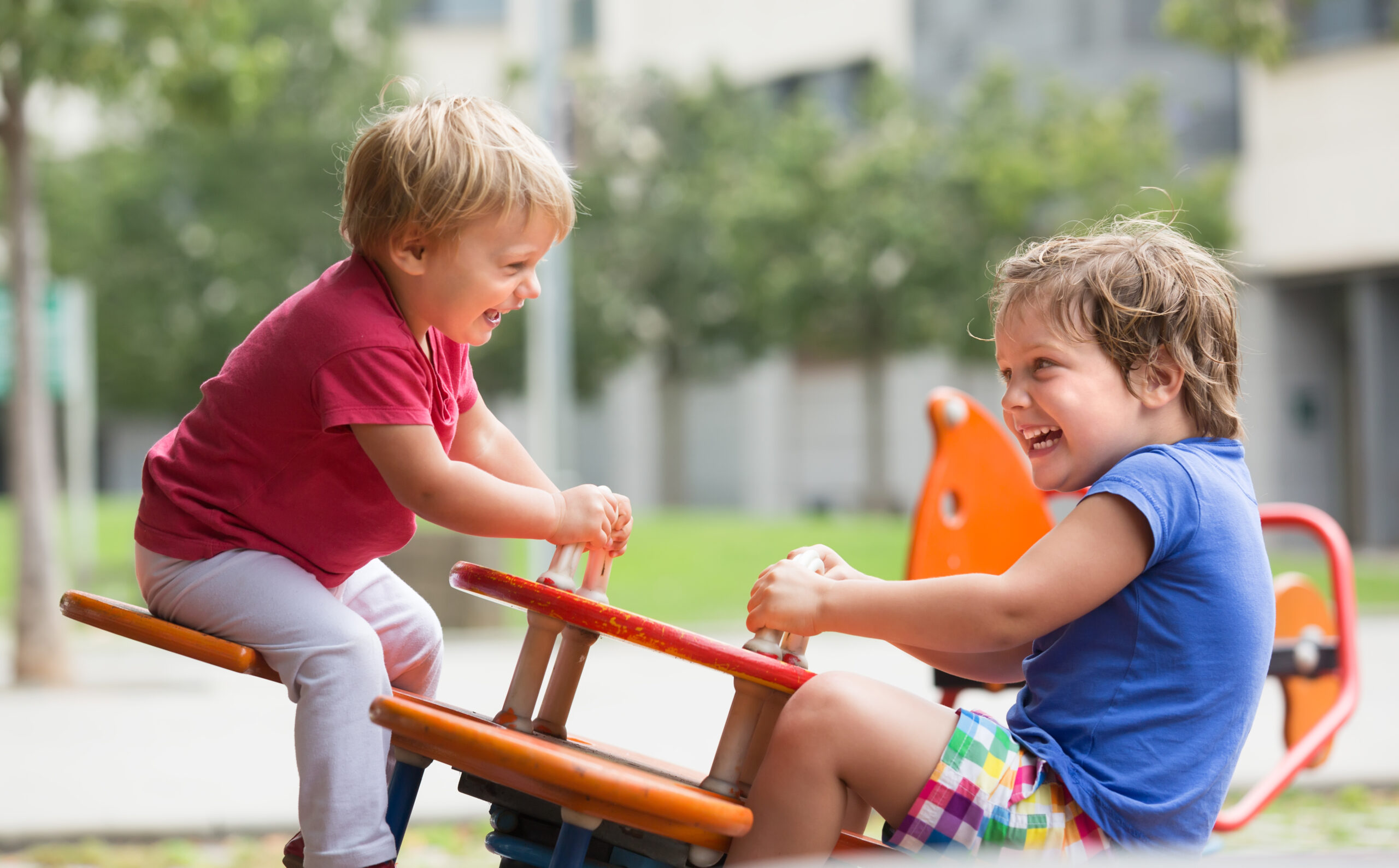 Two young boys in playground playing together on seesaw